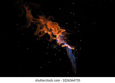blue and orange flame surrounded by sparkes emitting from the same source with a black background