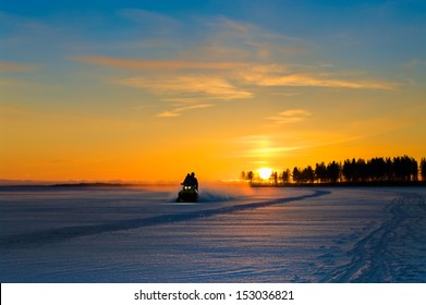 Blue and orange sunset on winter snowy lake and snowmobile with people on it. - Powered by Shutterstock