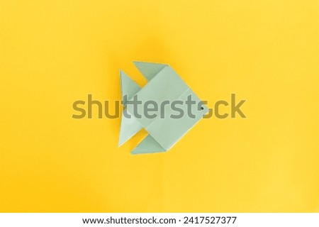 A blue origami fish with a drawn eye, set against a stark yellow background, perfect for an April Fools' Day theme. [[stock_photo]] © 