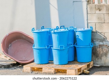 Blue pail with lids stacked on pallet beside exterior wall of industrial building.