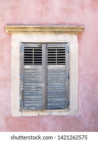 Blue painted window shutters set inside a pink wall of a house. Image has copy space.