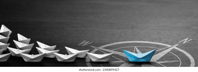 Blue Paper Boat With Compass Icon Leading A Fleet Of Small White Boats On Modern Black Wooden Table - Leadership Concept
					