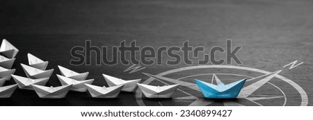 Blue Paper Boat With Compass Icon Leading A Fleet Of Small White Boats On Modern Black Wooden Table - Leadership Concept
