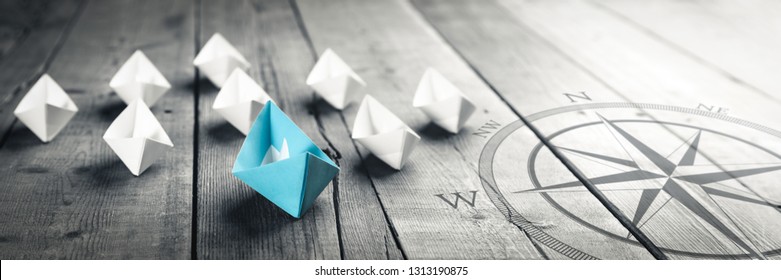 Blue Paper Boat Leading A Fleet Of Small White Boats With Compass Icon On Wooden Table With Vintage Effect - Leadership Concept	