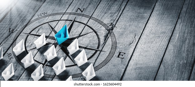 Blue Paper Boat Leading A Fleet Of Small White Boats With Compass Icon On Wooden Table With Sunlight - Leadership Concept - Shutterstock ID 1623604492