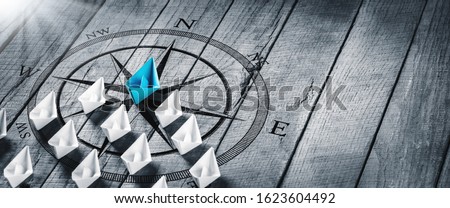 Blue Paper Boat Leading A Fleet Of Small White Boats With Compass Icon On Wooden Table With Sunlight - Leadership Concept