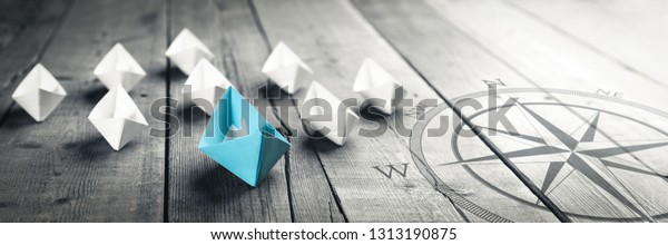 Blue Paper Boat Leading A Fleet Of Small White\
Boats With Compass Icon On Wooden Table With Vintage Effect -\
Leadership Concept	