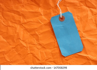 Blue Paper Luggage Or Price Tag On A Background Of Wrinkled Orange Paper With Room For Your Text