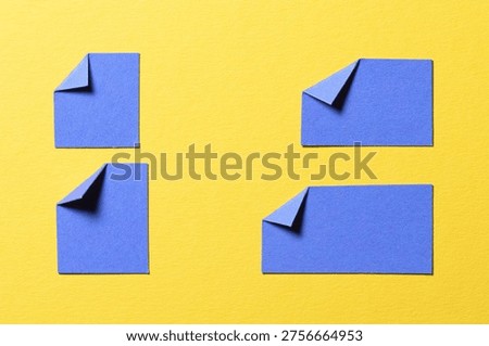 Blue paper message notes or sheets with folded edge dog-ear earmark and copy space for text on yellow background, top view flat lay conceptual desk backdrop