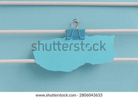 A blue paper note clipped to white rods against a light blue background. The scene is minimalistic and emphasizes organization and simplicity.