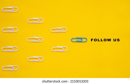 Blue paperclip leads white paperclips with the follow us message. Social media or internet followers concept.