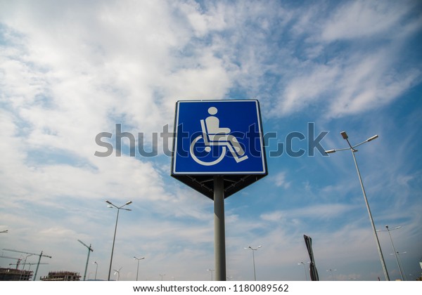 Blue parking sign for\
disabled persons on local mall parking lot, blue sky with white\
clouds background.