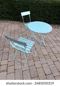 A Blue Patio Set With A Table And Two Chairs All In Front Of A Green Hedge.