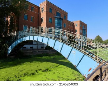 Blue Pedestrian Bridge Over Duckweed Covered River Foss In York, England. Health And Safety Executive Building Behind. 