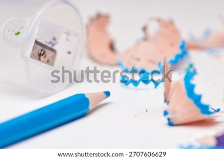 Blue pencil being sharpened, generating wood shavings and dust on a white background