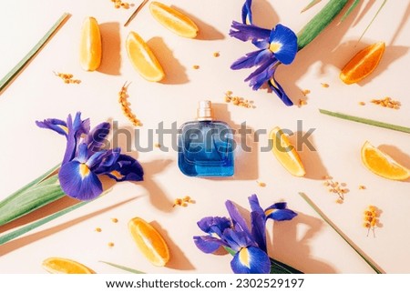 Blue perfume bottle, iris flowers and orange slices on beige background in sunlight. Top view, flat lay.
