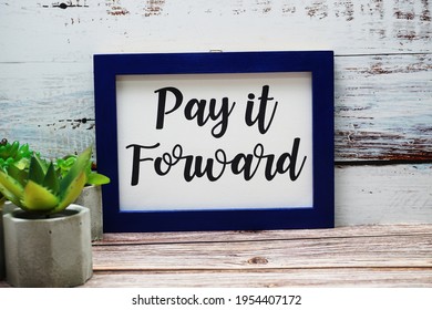 Blue Photo Frame With Pay It Forward Written And Small Cactus Decoration On Wooden Background