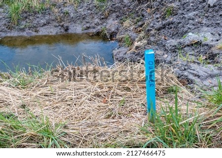 A blue picket post in a residential area under construction with the indication at which distance a culvert is located.