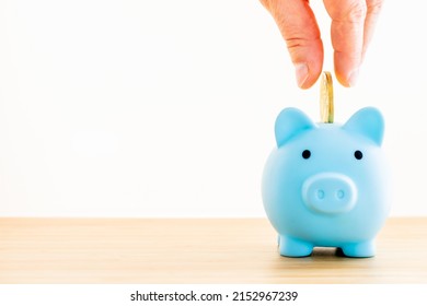 A Blue Piggy Bank On A White Background, Hand Tossing A Gold Coin Inside