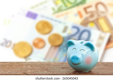 Blue Piggy Bank On Wooden Table Over Blurred  Banknote Background,money And Saving Concept.