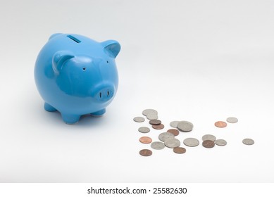 A blue piggy bank with some coins scattered next to it.