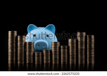 Blue piggy bank and stacked coins in denominations of 100 Kazakhstani tenge on a black background