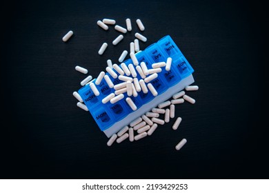 A Blue Pill Box On A Black Table With Scattered Pills.