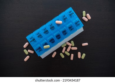 Blue Pill Box On A Black Table With Scattered Pink And Green Pills