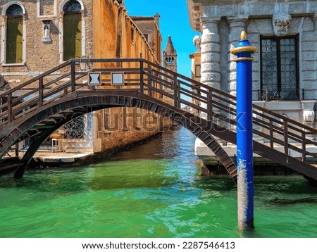 Blue pillar and small wooden bridge over the canal with beautiful green water in Venice, Italy.