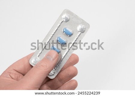 Blue pills for treating erectile dysfunction or impotence, being held in hand. Pills in foil.