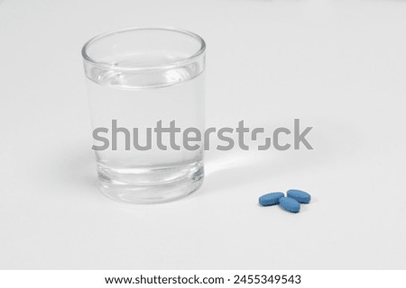 Blue pills for treating erectile dysfunction on a white table with glass of water