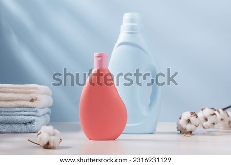 Blue and pink plastic bottle of laundry detergent with cotton towels and branch of cotton in the background. Delicate wash concept