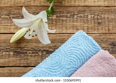 Blue And Pink Soft Terry Towels With White Lily Flower On Old Wooden Boards. Top View.