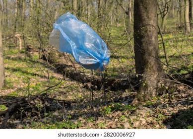 Blue plastic bag full of collected litter captured mid-air while falling or thrown in sunny spring forest. Powerful conceptual image for plastic pollution, illegal dumping and environmental awareness campaigns