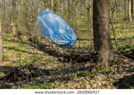 Blue plastic bag full of collected litter captured mid-air while falling or thrown in sunny spring forest. Powerful conceptual image for plastic pollution, illegal dumping and environmental awareness campaigns