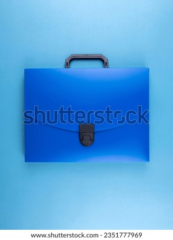 Blue plastic  briefcase folder for documents and school items on a bright blue table