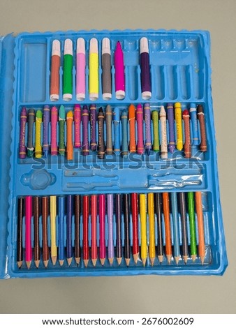 A blue plastic case filled with various art supplies.  Crayons, colored pencils, and markers are neatly organized in the compartments. The case is likely for children's art activities.