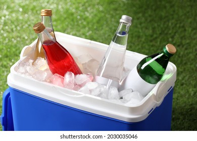 Blue Plastic Cool Box With Drinks And Ice Cubes On Green Grass