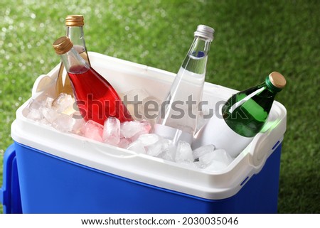 Blue plastic cool box with drinks and ice cubes on green grass