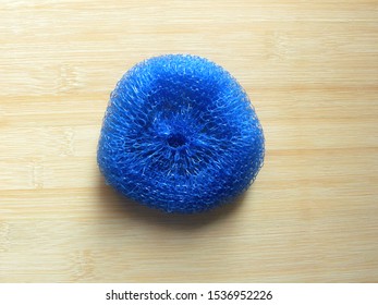 Blue plastic dish scrubber kept on wooden table - Powered by Shutterstock