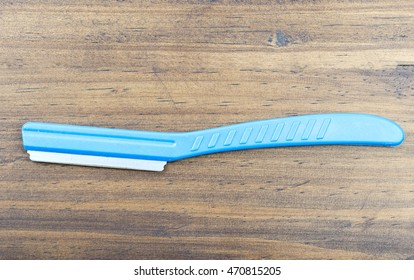 A Blue Plastic Handle Of A Razor Which Just Shaved Of Women Eyebrow On Wooden Ground