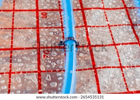Blue plastic pipe being fixed on insulation panel during underfloor heating system installation, ensuring thermal efficiency in modern construction