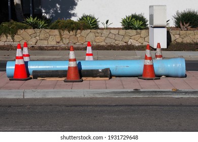 Blue Plastic Pipe And A Black Metal Pipe For Main Water Line Construction On A City Street With Warning Traffic Cones Around