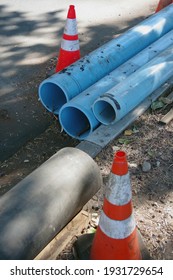 Blue Plastic Pipe And A Black Metal Pipe For Main Water Line Construction On A City Street With Warning Traffic Cones