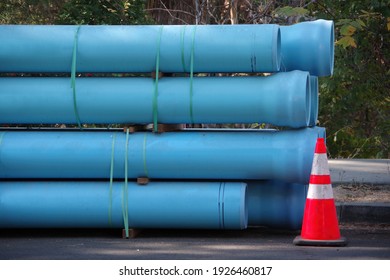 Blue Plastic Pipes For Main Water Line Construction Stacked On A City Street With A Warning Traffic Cone