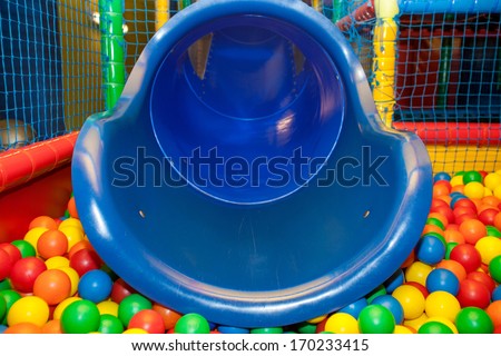 Blue plastic slide and pool covered with colourful balls in the kid's playground.