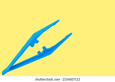 Blue Plastic Sterile Surgical Tweezers Isolated On Yellow Background.