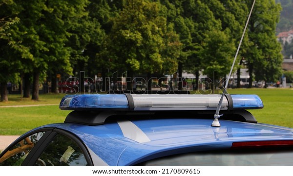 Blue police car\
sirens as they patrol the public park looking for criminals and\
trees in the background