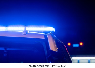 Blue police lights on a car at night with red traffic stoplight in the background - Shutterstock ID 1944624055