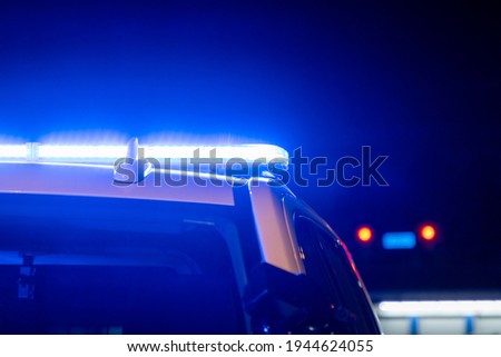 Blue police lights on a car at night with red traffic stoplight in the background